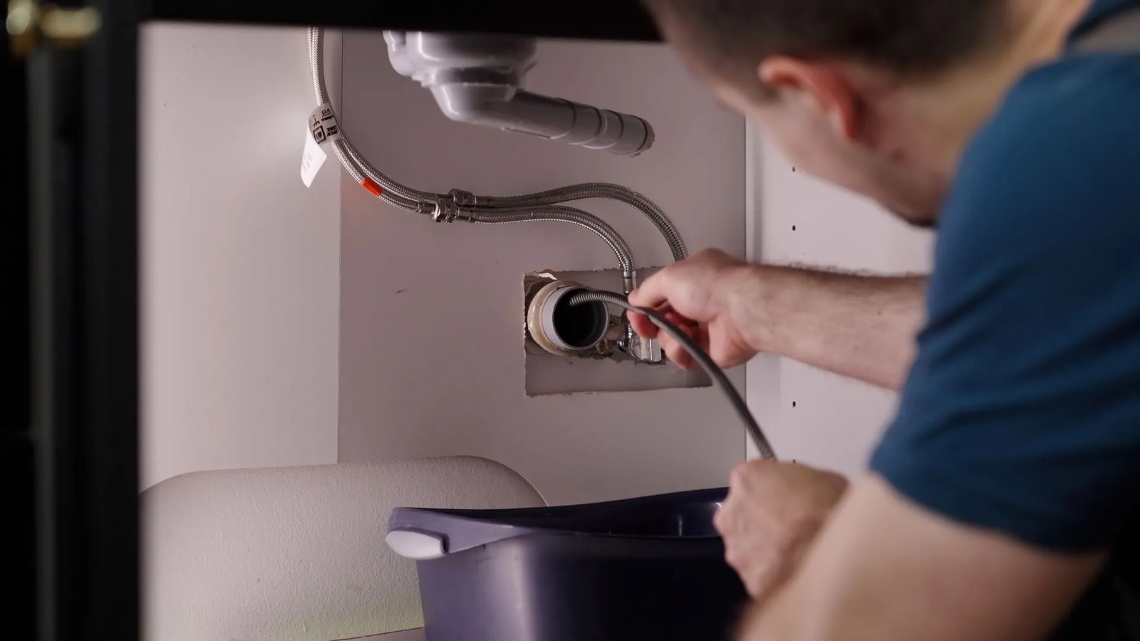 Drain technician feeding a clearing cable into a kitchen sink drain line